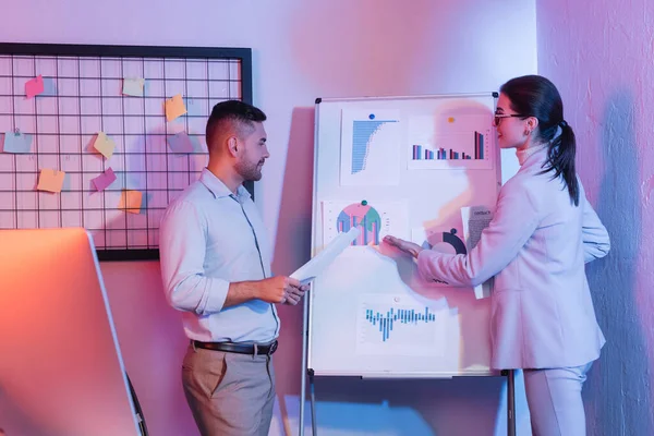 Homme d'affaires regardant femme d'affaires pointant avec la main au tableau à feuilles avec des graphiques et des graphiques — Photo de stock