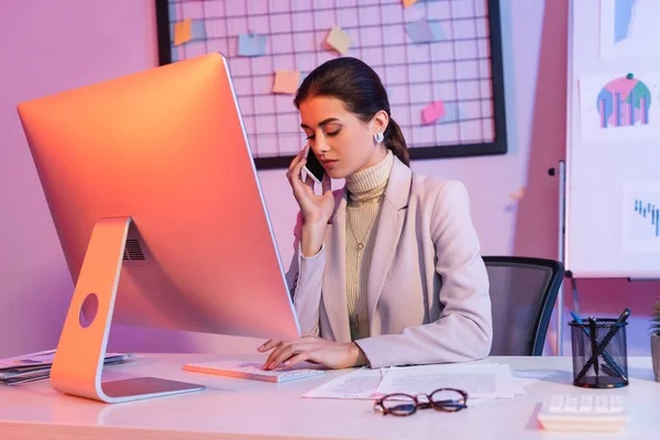 Donna d'affari che parla su smartphone e guarda la tastiera del computer in ufficio — Foto stock