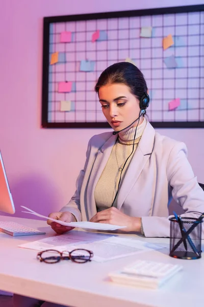 Female operator in headset looking at documents in office — Stock Photo