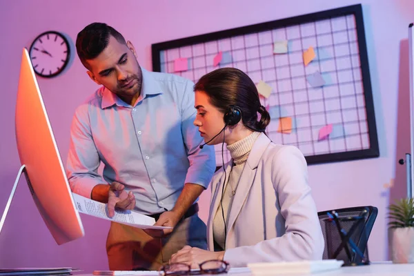 Empresario señalando con el dedo en el contrato cerca de operador femenino en auriculares - foto de stock