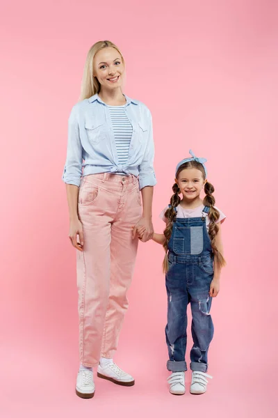 Full length of happy mother and daughter holding hands and standing on pink — Stock Photo