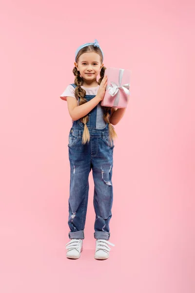 Full length of happy kid smiling and holding present on pink — Stock Photo