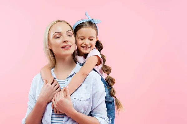 Bambino felice con gli occhi chiusi abbracciando allegra madre isolata su rosa — Foto stock