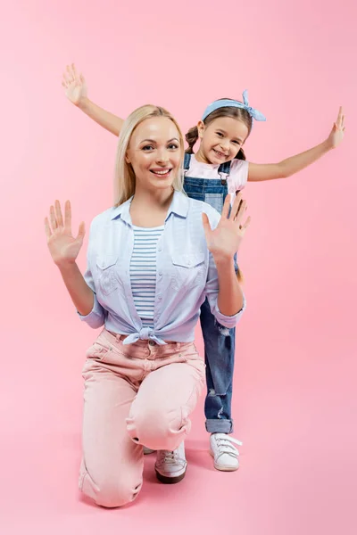 Glückliches Kind mit ausgestreckten Händen, das hinter der Mutter auf rosa steht — Stockfoto