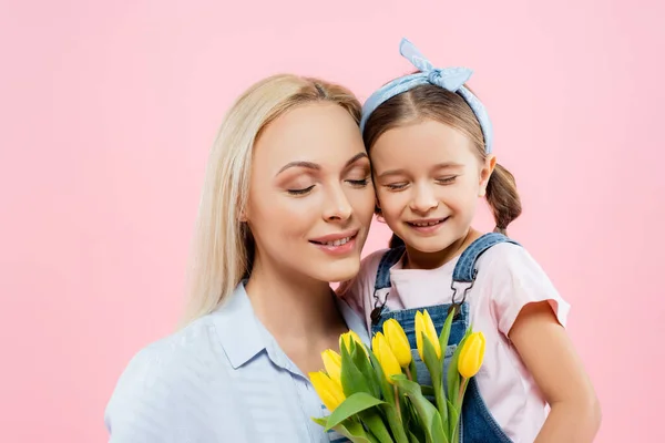 Happy mother and daughter with closed eyes smiling near tulips isolated on pink — Stock Photo