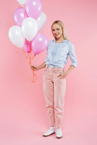 Glückliche Frau steht mit der Hand in der Tasche und hält Luftballons auf rosa — Stockfoto