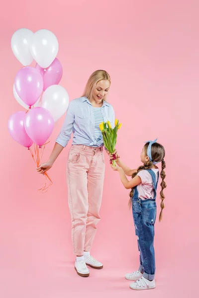 Niño dando tulipanes a madre feliz de pie con globos en rosa - foto de stock