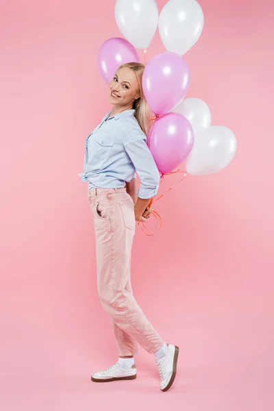 Pleine longueur de femme gaie debout et tenant des ballons sur rose — Photo de stock