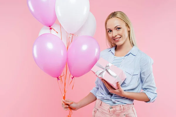 Mulher feliz segurando balões e caixa de presente isolado em rosa — Fotografia de Stock