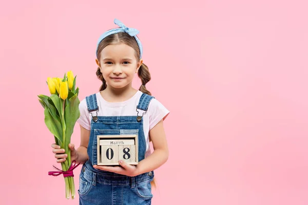 Niño feliz sosteniendo tulipanes y cubos de madera con 8 letras de marzo aisladas en rosa - foto de stock