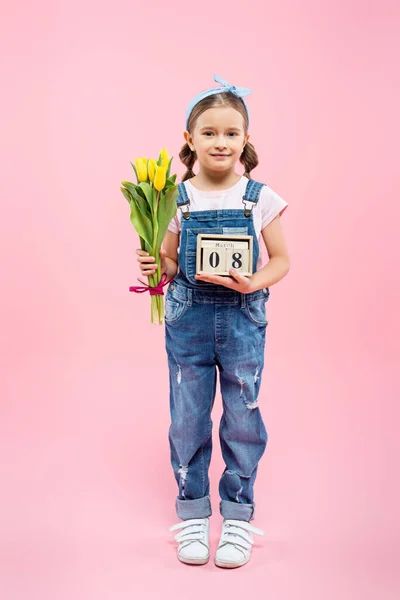 Longitud completa de niño feliz sosteniendo tulipanes y cubos de madera con 8 letras de marzo en rosa - foto de stock