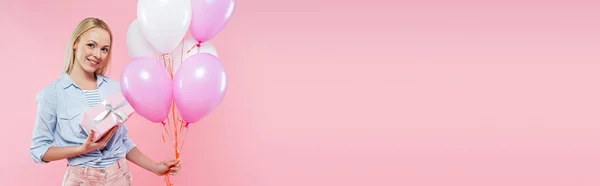 Glückliche Frau hält Luftballons und Geschenkbox isoliert auf rosa, Banner — Stockfoto