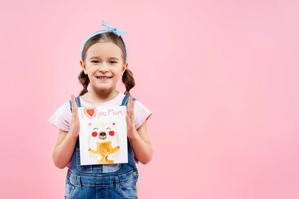 Glückliches Kind hält Grußkarte mit Ich liebe dich Mama Schriftzug isoliert auf rosa — Stockfoto