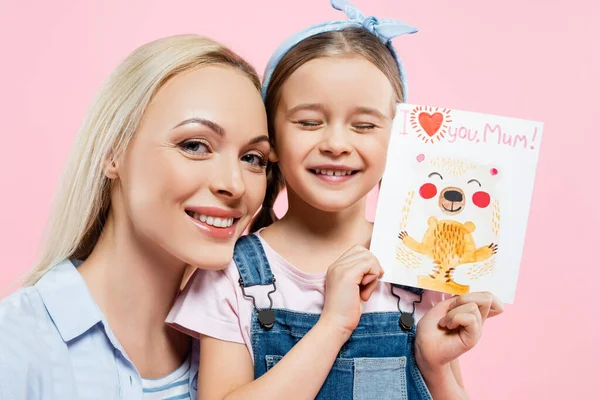 Glückliches Kind hält Grußkarte mit Ich liebe dich Mama Schriftzug in der Nähe Mutter isoliert auf rosa — Stockfoto