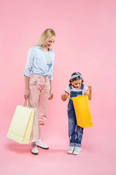 Longitud completa de la madre y la hija alegre mirando el bolso de compras en rosa - foto de stock