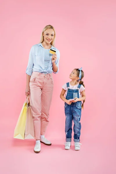 Повна довжина матері тримає кредитну картку і сумки біля дочки з смартфоном на рожевому — стокове фото