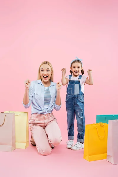 Longitud completa de la madre y la hija emocionados cerca de bolsas de compras en rosa - foto de stock
