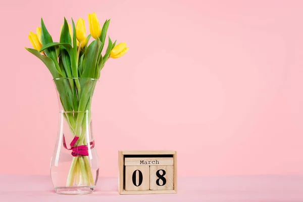 Деревянный календарь с 8 мартовскими надписями возле вазы с тюльпанами на розовом — стоковое фото