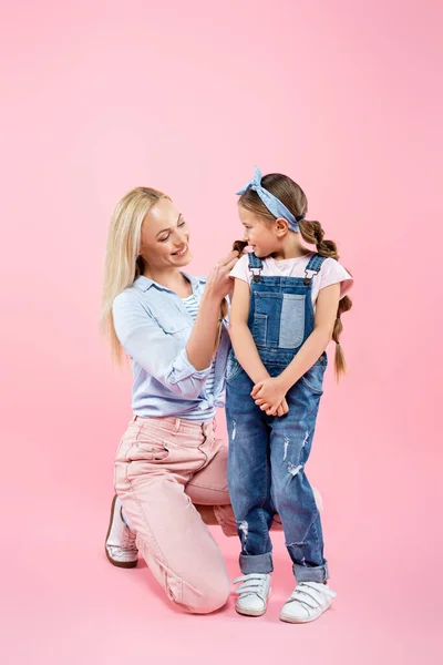 La longitud completa de la mamá feliz que trenza el cabello de la hija en rosado - foto de stock