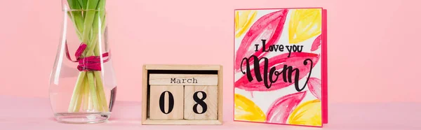 Wooden calendar with 8 march lettering near greeting card and vase with flowers on pink, banner — Stock Photo