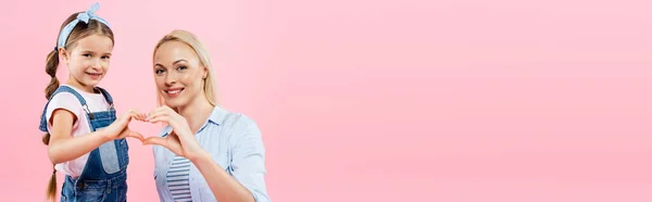 Happy mother and daughter showing heart sign with hands isolated on pink, banner — Stock Photo