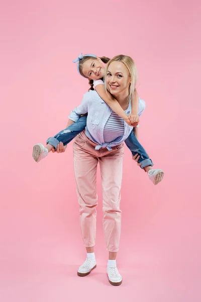 Longitud completa de feliz madre piggybacking hija en rosa — Stock Photo