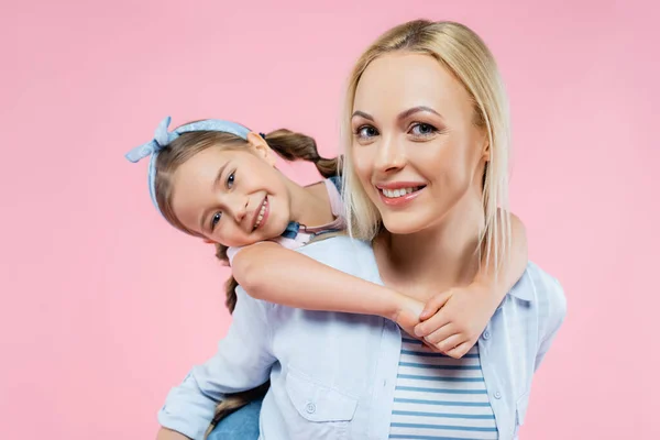Fröhliches Kind umarmt glückliche Mutter und blickt isoliert in die Kamera auf rosa — Stockfoto