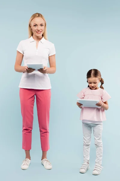 Longitud completa de alegre madre e hija sosteniendo tabletas digitales en azul - foto de stock