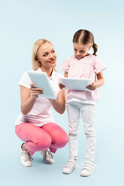 Pleine longueur de mère et fille heureux tenant des comprimés numériques sur bleu — Photo de stock