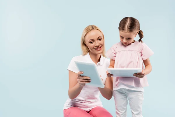 Щаслива мати і дочка тримають цифрові планшети ізольовані на синьому — стокове фото