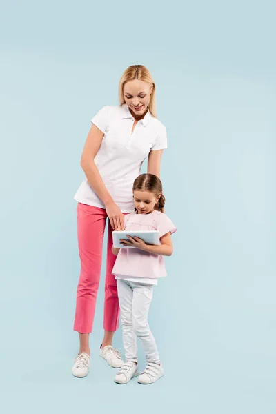 Comprimento total de mãe feliz e filha olhando para tablet digital em azul — Fotografia de Stock