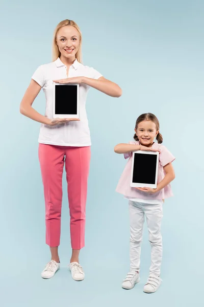 Full length of happy mother and daughter holding digital tablets with blank screen on blue — Stock Photo