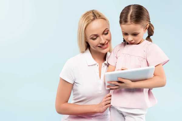 Feliz madre e hija mirando tableta digital aislada en azul - foto de stock