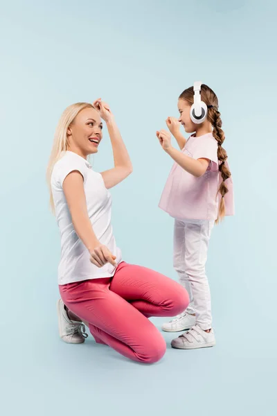 Glückliches Kind in drahtlosen Kopfhörern tanzt mit Mutter auf blau — Stockfoto