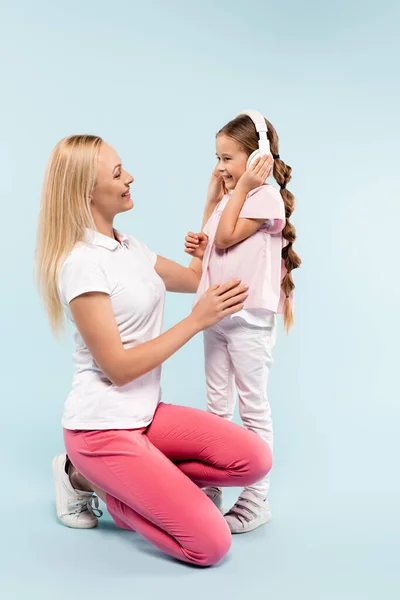 Happy kid in wireless headphones looking at smiling mother on blue — Stock Photo