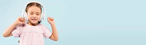 Niño feliz con los ojos cerrados en auriculares inalámbricos sonriendo aislado en azul, bandera - foto de stock