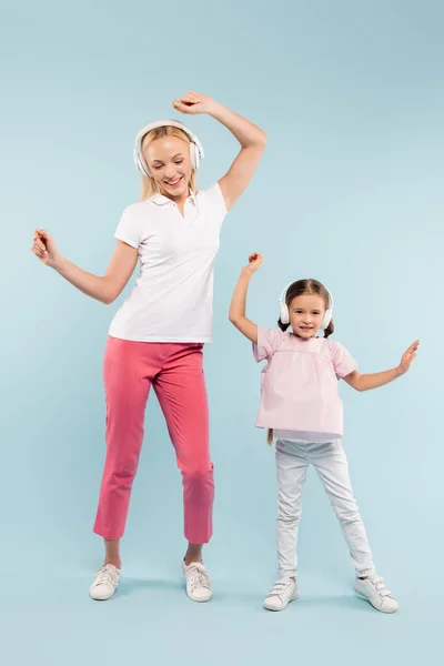 In voller Länge fröhliche Mutter und Kind in drahtlosen Kopfhörern tanzen auf blau — Stockfoto