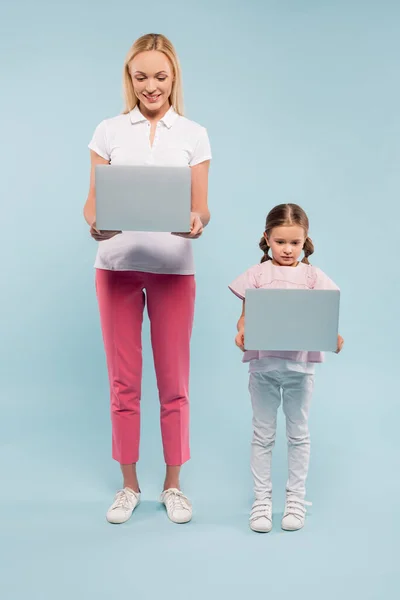 Повна довжина матері і дочки, що стоїть з ноутбуками на синьому — стокове фото