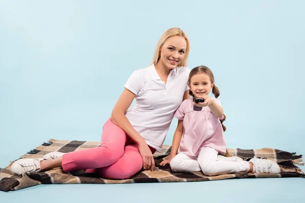 Lächelnde Mutter und Tochter auf Decke sitzend und Film auf blau anschauend — Stockfoto
