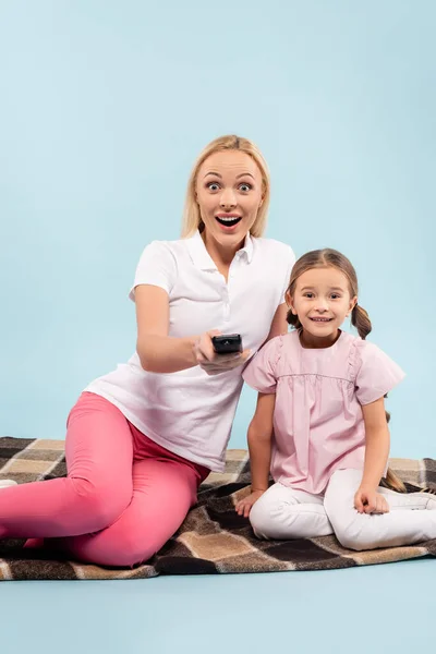 Amazed mother and daughter sitting on blanket and watching movie on blue — Stock Photo