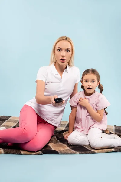 Shocked mother and daughter sitting on blanket and watching movie on blue — Stock Photo