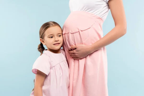 Happy daughter standing with pregnant mother isolated on blue — Stock Photo