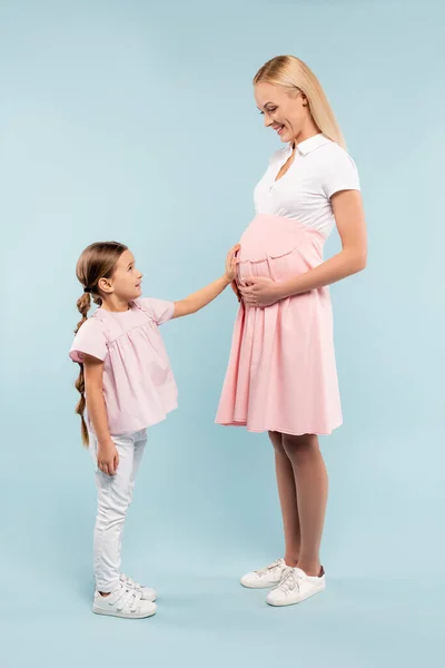 Full length of daughter touching belly of pregnant mother on blue — Stock Photo