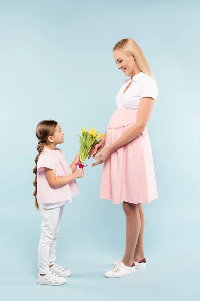 Full length of daughter holding tulips near happy pregnant mother on blue — Stock Photo