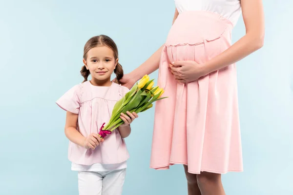 Happy kid holding tulips near pregnant mother isolated on blue — Stock Photo