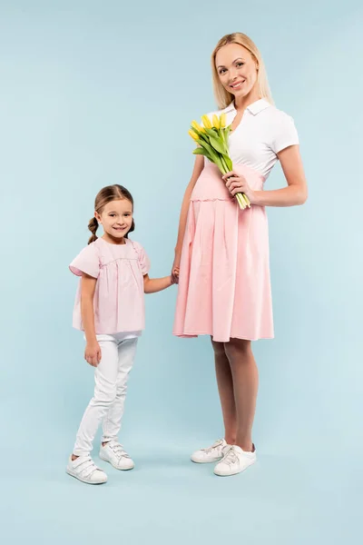 Lunghezza piena di bambino che si tiene per mano con madre incinta con tulipani su azzurro — Foto stock