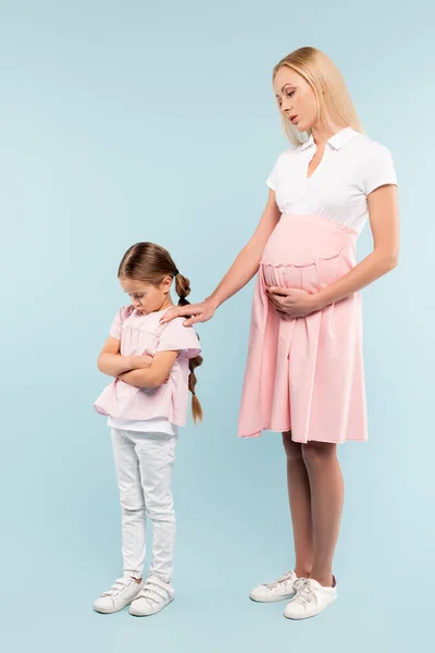 Offended daughter standing with pregnant mother on blue — Stock Photo