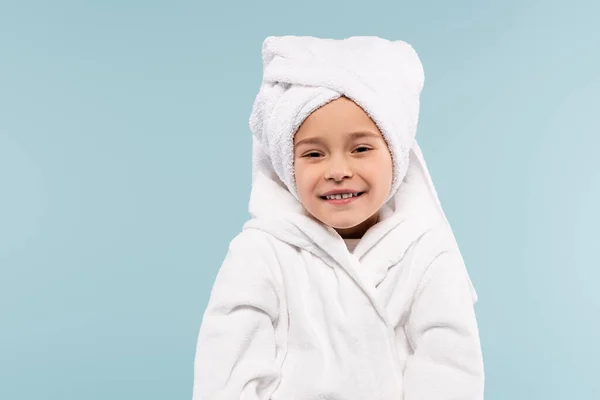 Niño feliz en albornoz envuelto en toalla sonriendo aislado en azul - foto de stock