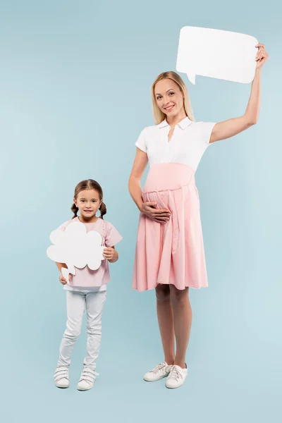 Full length of pregnant mother and happy kid holding thought and speech bubbles on blue — Stock Photo
