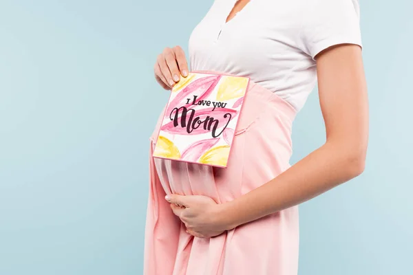 Vista ritagliata di donna incinta in possesso di biglietto di auguri con ti amo mamma lettering isolato su blu — Foto stock